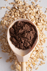 Ground cocoa in a wooden spoon against the background of oatmeal. Ingredients for the preparation of a healthy cocktail drink