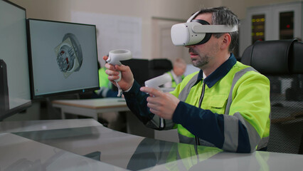 Mature industrial engineer in vr headset working on 3d model using computer and joysticks