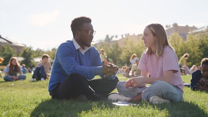 African-American helping girl during outdoor lesson with college students on lawn in park