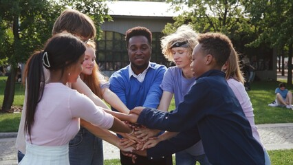 African-American teacher and teen students put hands together and hug outside school
