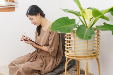 Relaxation lifestyle concept, Young Asian woman writing on notebook while sitting in living room