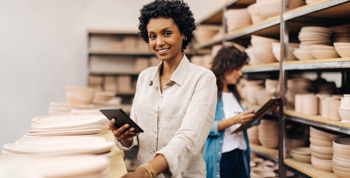 Cheerful female ceramist using a digital tablet in her shop - Powered by Adobe