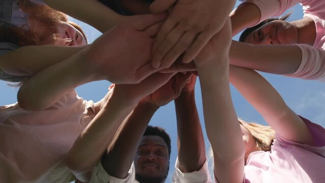 Bottom view of young diverse people putting their hands together outdoors. 