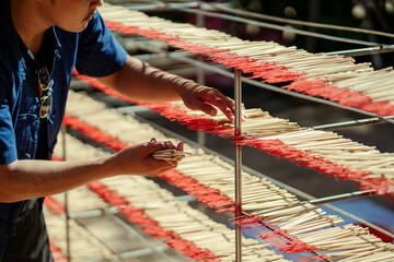 Selective focus. Hand indigenous young Asian man working make dried incense stick product on shelf. Southeast asia culture and tourism. Incense sticks SME business.