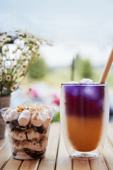 Trendy purple and yellow cocktail with straw reed. Light dessert with nuts in a disposable cup. Anchan blue tea - antioxidants and detox water at the terrace on the wooden table