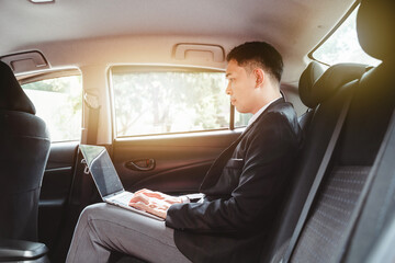 Fototapeta na wymiar Young Asian businessman using a laptop in the backseat of a car.