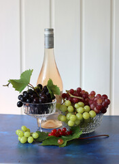 Still life with wine and grapes. Colorful photo of bottle of rose wine and different sorts of grapes. Seasonal fruit on a table. 