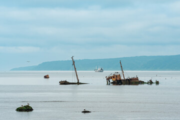 remains of a sunken ship against the backdrop of a sea bay with foggy mountains in the background