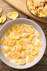 Tasty cornflakes with milk in bowl on wooden table, flat lay