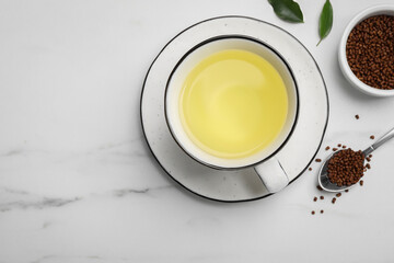 Cup of buckwheat tea and granules on white marble table, flat lay. Space for text