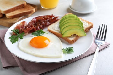 Romantic breakfast with fried bacon, heart shaped egg and avocado toast on light grey table, closeup. Valentine's day celebration