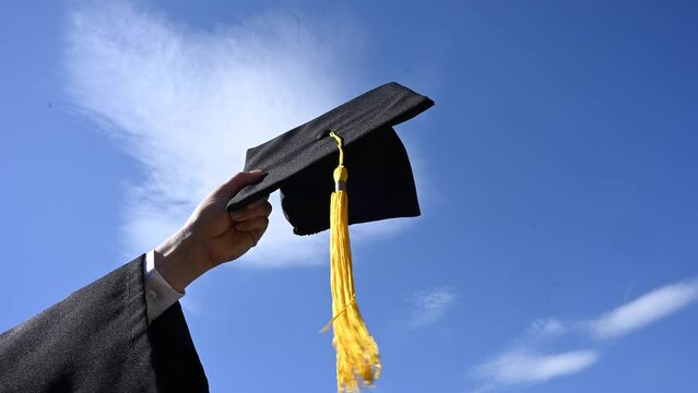 Close-up of a woman's hand with a graduation cap against the blue sky. 