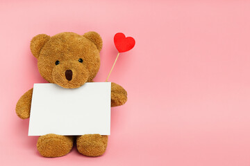 Cute teddy bear with red heart and blank card on pink background, space for text. Valentine's day...