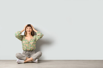 Fototapeta na wymiar Happy young girl sitting on floor near white wall. Space for text
