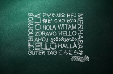 Greeting words in different foreign languages written on green chalkboard - obrazy, fototapety, plakaty
