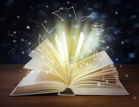 Open book on wooden table and illustration of zodiac wheel with astrological signs