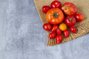 Fresh ripe different varieties of garden tomatoes on crumpled brown burlap,  still life 