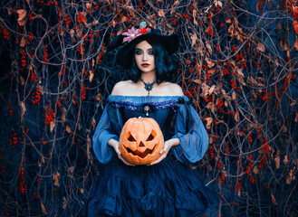 Fantasy woman luxurious medieval witch holding carved jack-o'-lantern pumpkin in hands. Sexy girl...