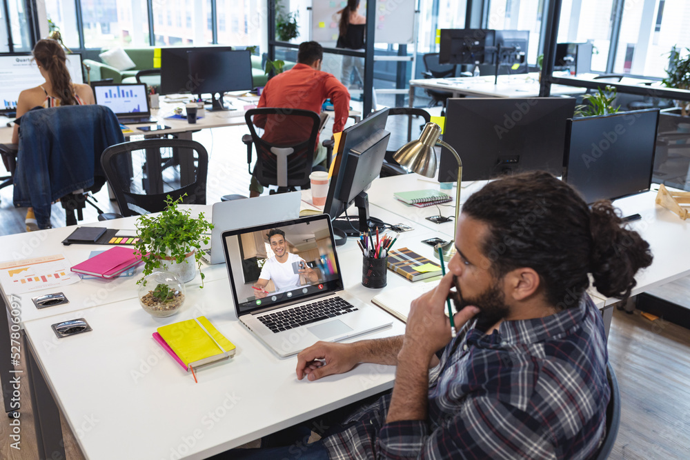 Sticker Biracial businessman discussing work with male colleague while video calling through laptop