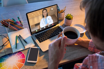 Caucasian businessman having coffee during video conference with asian female doctor