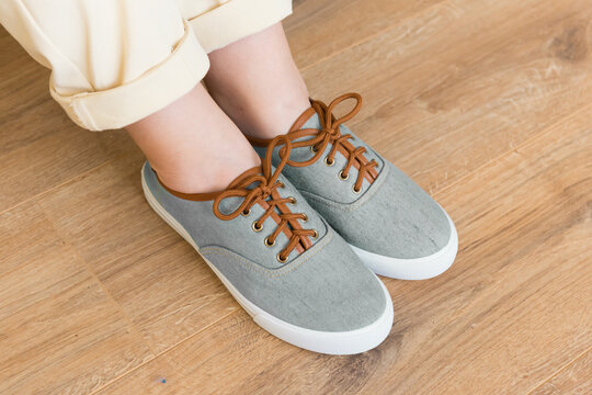 Casual grey shoes sneakers on woman feet on wooden floor