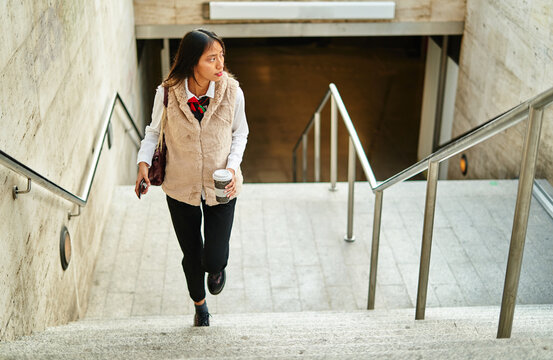 Hispanic woman with coffee walking upstairs in metro