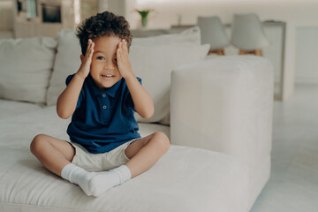 Cute little boy with curly hair enjoying game of hide and seek at home