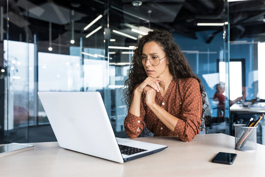 Pensive and focused female programmer web developer working in modern product development company Hispanic woman sitting and thinking using laptop to write code.