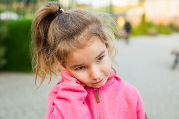 A little girl in a pink hoodie with a sad and tearful face is holding her ear. Ear pain, otitis...