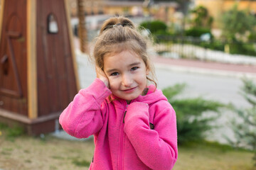 A little girl in a pink hoodie with a sad and tearful face is holding her ear. Ear pain, otitis...