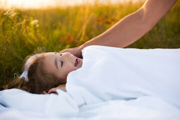 Girl sleeps on white bed in the grass, fresh air. Dad's hand gently pats his head. Care,...