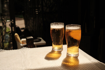 Two glasses of cold beer on the table of street cafe, beautiful shadows from bright sunlight. Copy space.