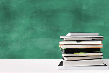 stack of books on white desk against green chalkboard with copy space, education and school concept
