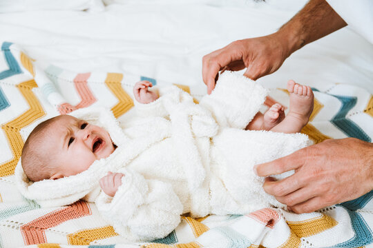 Crop father clothing baby crying in warm robe after bathing in light bedroom