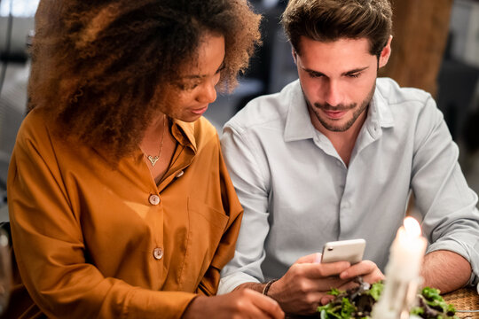 Cheerful young couple using smartphone at dinner
