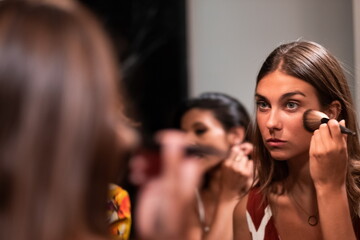 Cheerful young female friends refresh makeup in bathroom