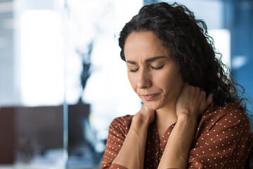 Hispanic woman overtired working in modern office businesswoman has severe neck pain, massages neck...