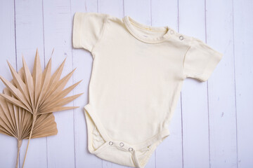 Yellow baby bodysuit mockup for logo, text or design on wooden background with palm leaves top view