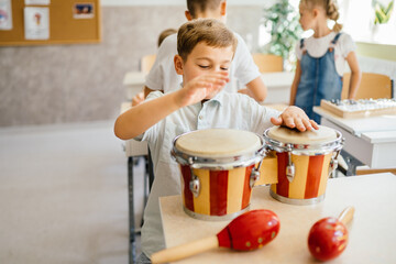 Cute little pupil boy play with drums at classroom Children with musical instruments at school.