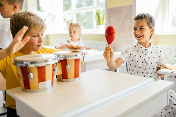 Group of five excited children boys and girls playing musical instruments at class.