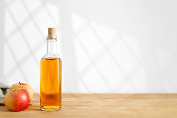 Homemade fresh Apple cider, vinegar, juice in glass bottle and fresh apples  on wooden table. Window shadow. Copy space.