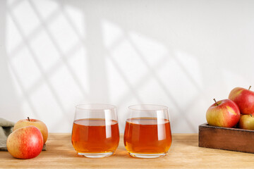Homemade fresh Apple cider, juice in two glasses and fresh apples on wooden table. Window shadow. Copy space.