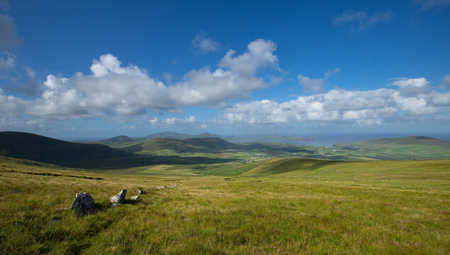 Vue spectaculaire montrant un paysage d'Irlande avec des collines, des prairies vertes et la mer, un ciel ensoleillé et nuageux