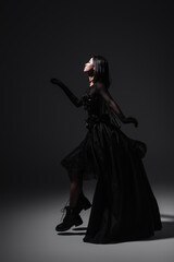 side view of asian young woman in black gothic dress and gloves levitating on dark grey.