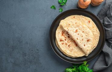 Fresh Indian chapati tortillas with fresh parsley on a graphite background. Top view, copy space