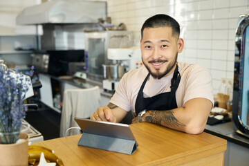 Fototapeta premium Friendly bearded barista looking inviting at coffee shop counter