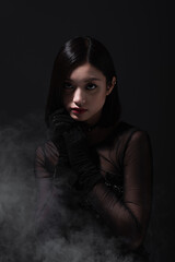 portrait of young asian woman in gothic outfit and gloves on grey with smoke.