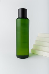 Green care cosmetics bottle mockup template, no label, no brand. Face skin toner, tonic with concrete stairs decor on white background