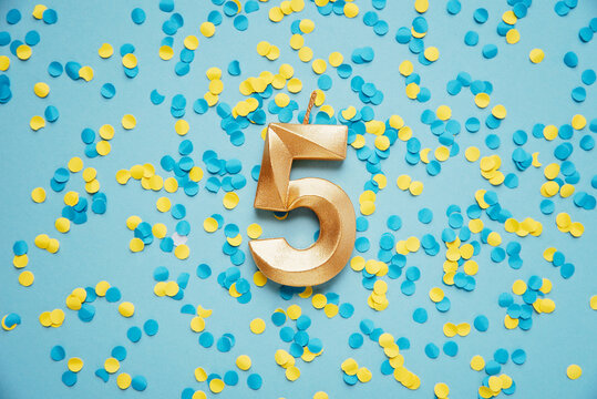 Number 5 five golden celebration birthday candle on yellow and blue confetti Background. five years birthday. concept of celebrating birthday, anniversary, important date, holiday