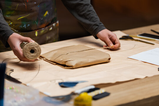 Cropped view of african american craftswoman holding twine near package in workshop.
